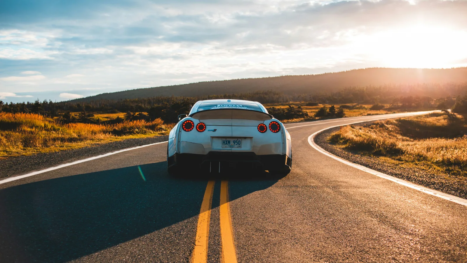 A silver sports car on a winding road at sunset.
